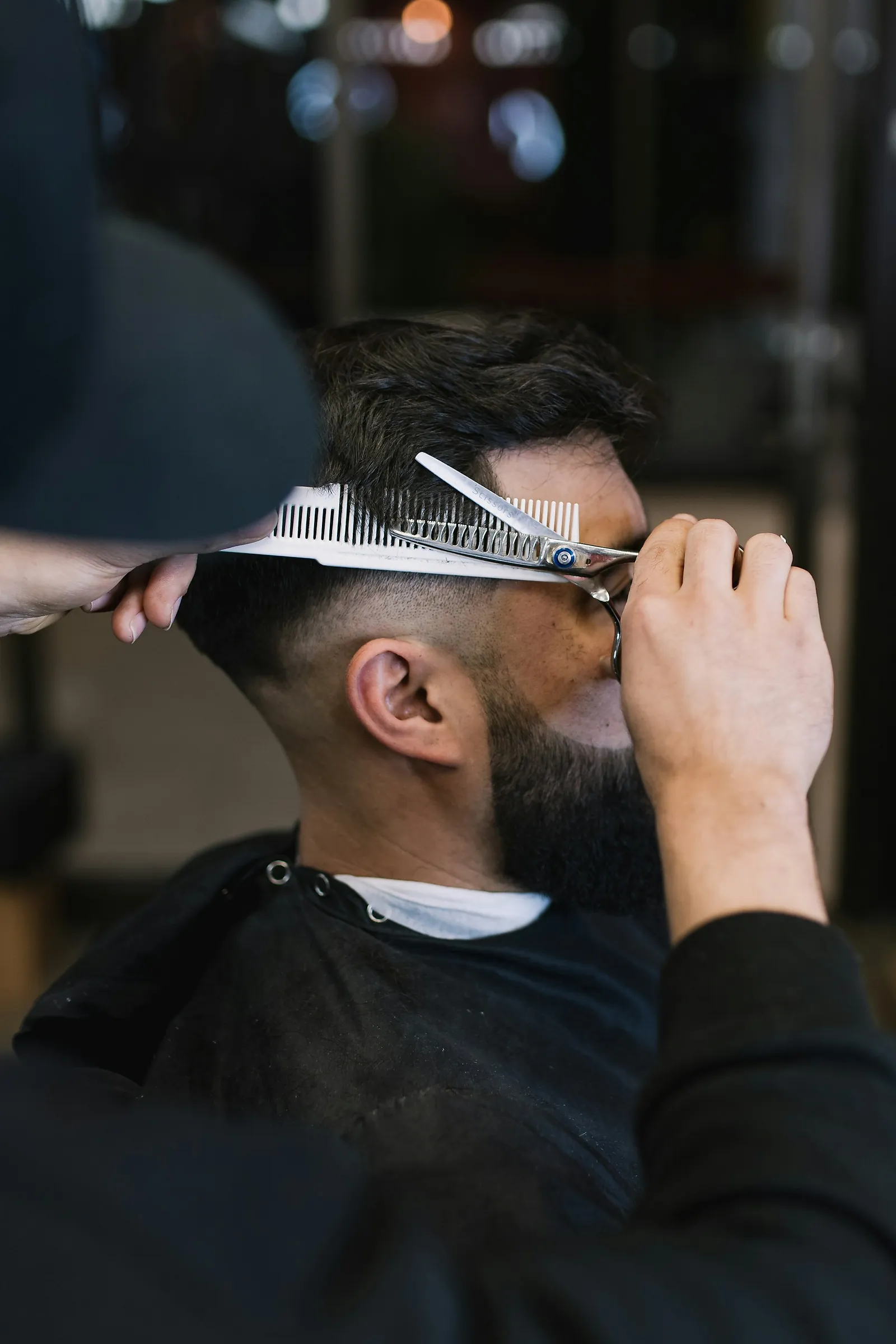 Coupe aux ciseaux et au peigne sur un homme barbu, en plein travail au studio